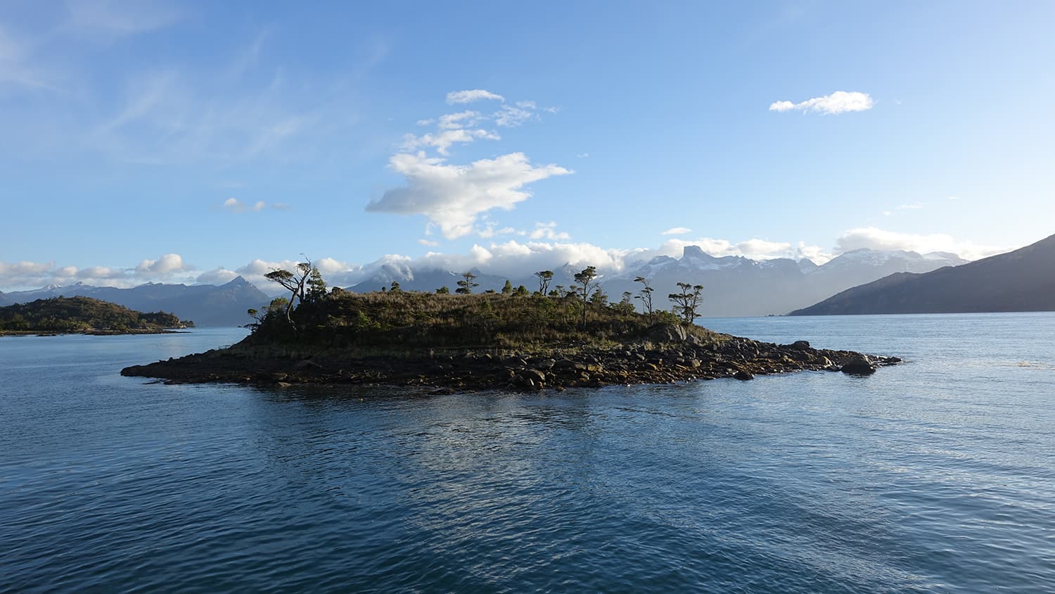 tiny island in the fjords of Tierra del Fuego with snow-capped mountains in the background